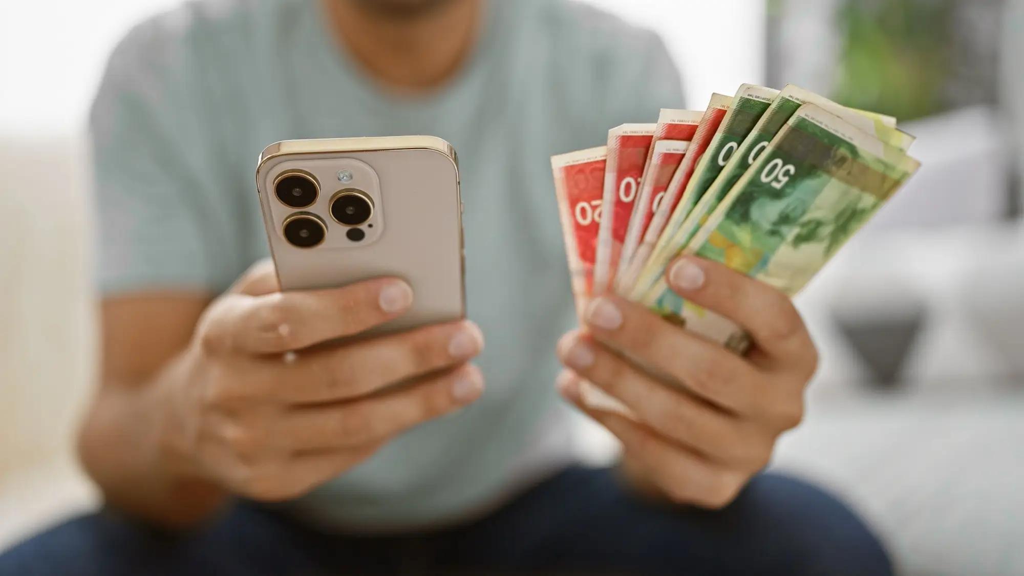 Muž s mobilem v ruce a penězi, šikovně investoval a tak se raduje ze zisku