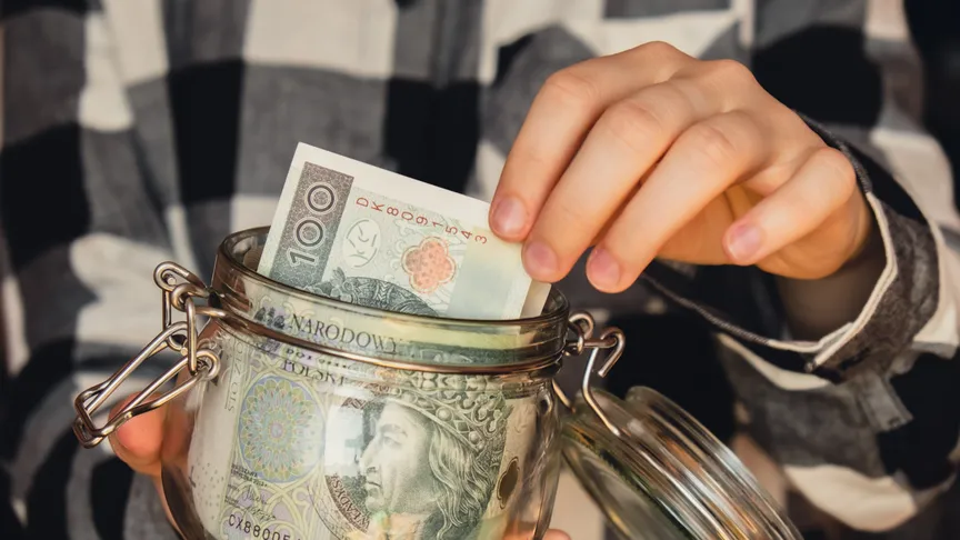 Postava v černobílé kostkované košili drží malou zavírací sklenici, z které vytahuje papírovou bankovku