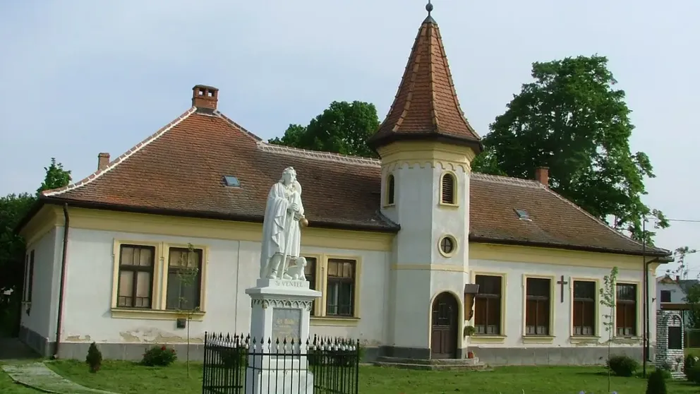 Světlý dům s červenou taškovou střechou, který se nachází v obci Chernelházadamonya. Stojí před ním jakási bílá socha.