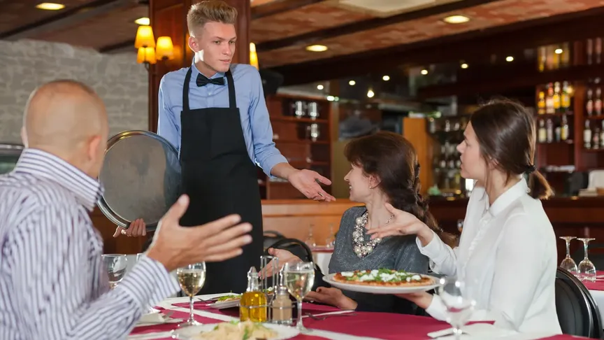 Obrázek ukazuje restauraci. U stolu zde sedí muž s dvěma ženami. Stojí nad nimi zmatený číšník. Očividně neochotný řešit jejich nespokojenost.