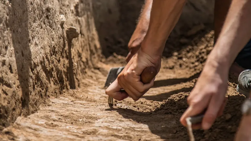 Archeologové pracují ve vykopané jámě a odhalují vrstvy země