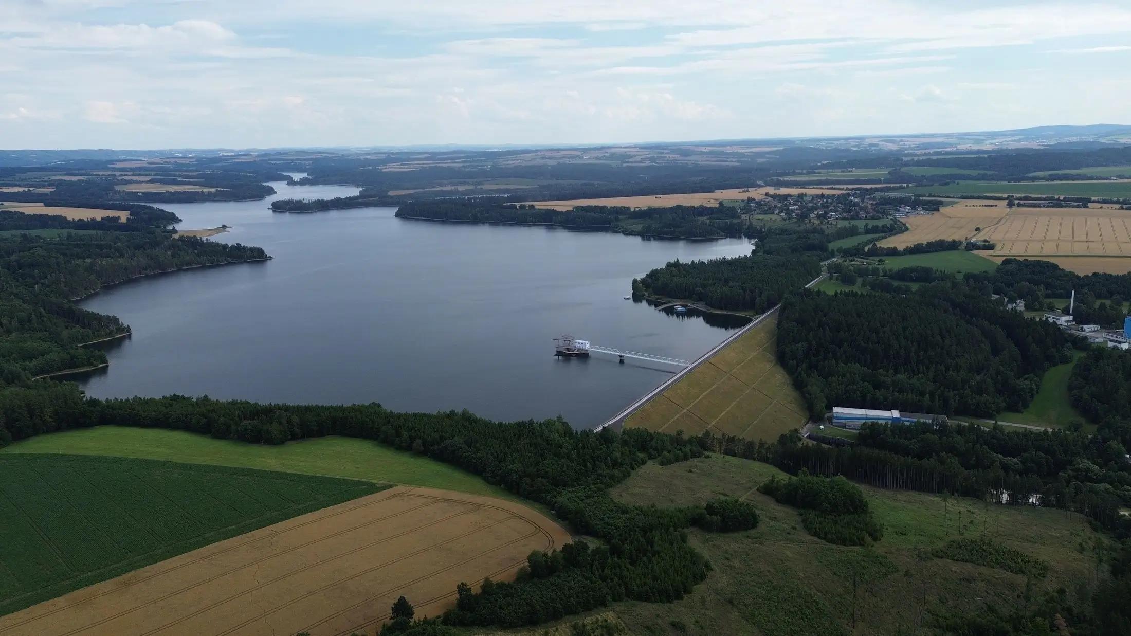 Letecký pohled na vodní nádrž Švihov. Vidět jde i její okolní pole a lesíky, které jsou zelené.