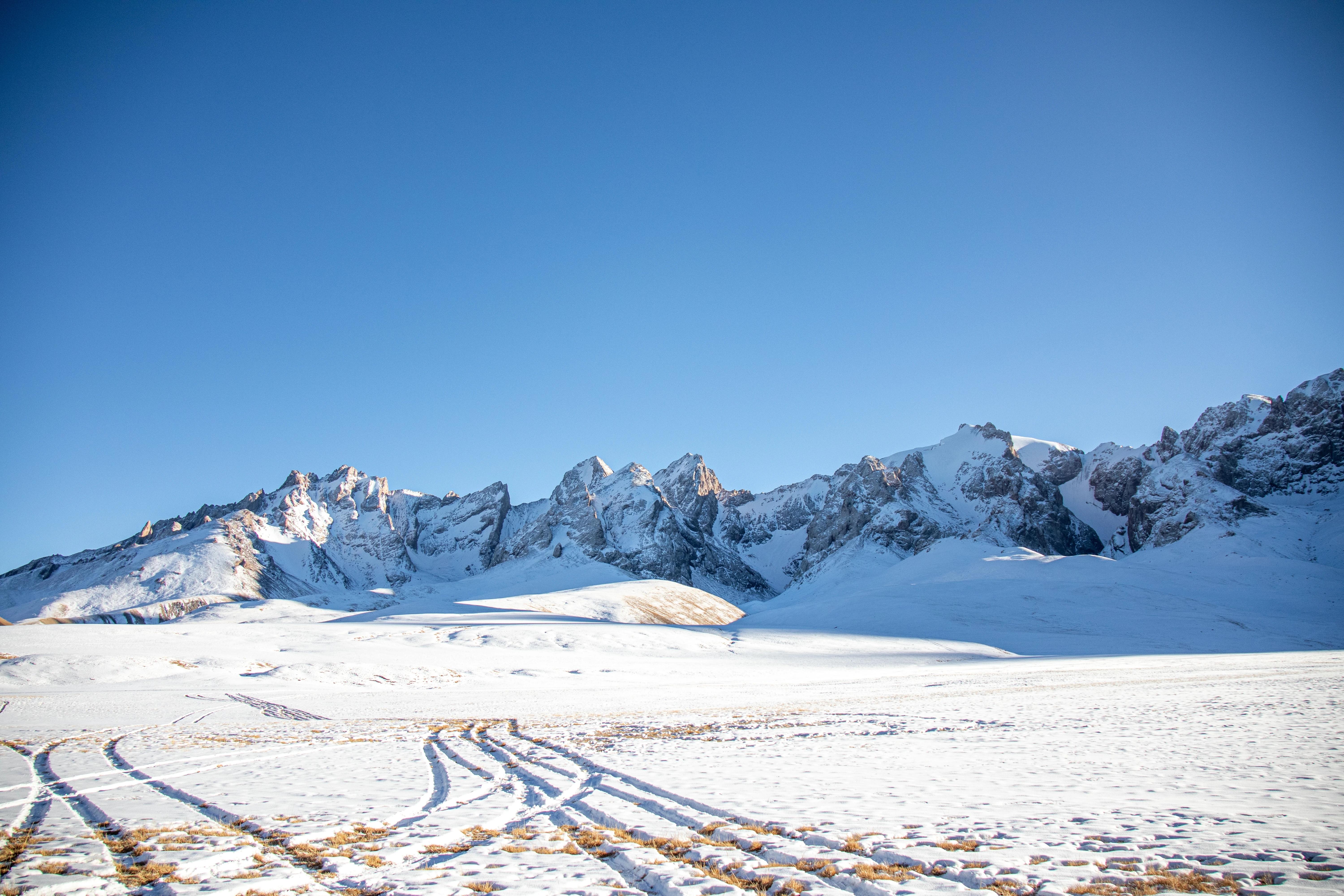 Zasněžená krajina, kde lze pozorovat hory a jasnou oblohu.