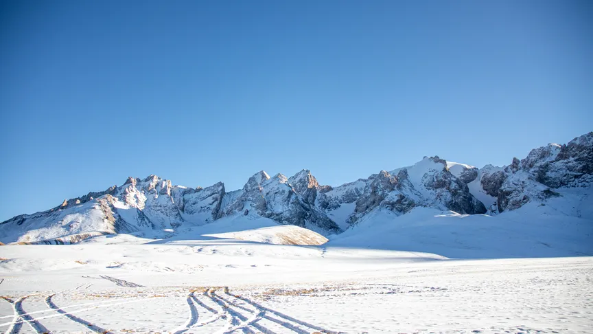 Zasněžená krajina, kde lze pozorovat hory a jasnou oblohu.