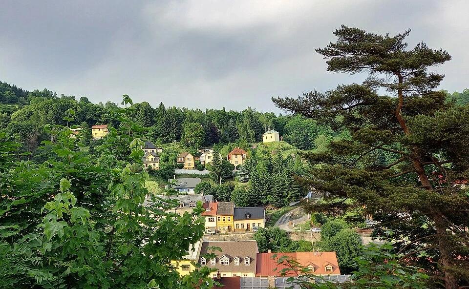 Pohle na město Jáchymov obklopené stromy. V pozadí se nachází kaple sv. Jana Nepomuckého