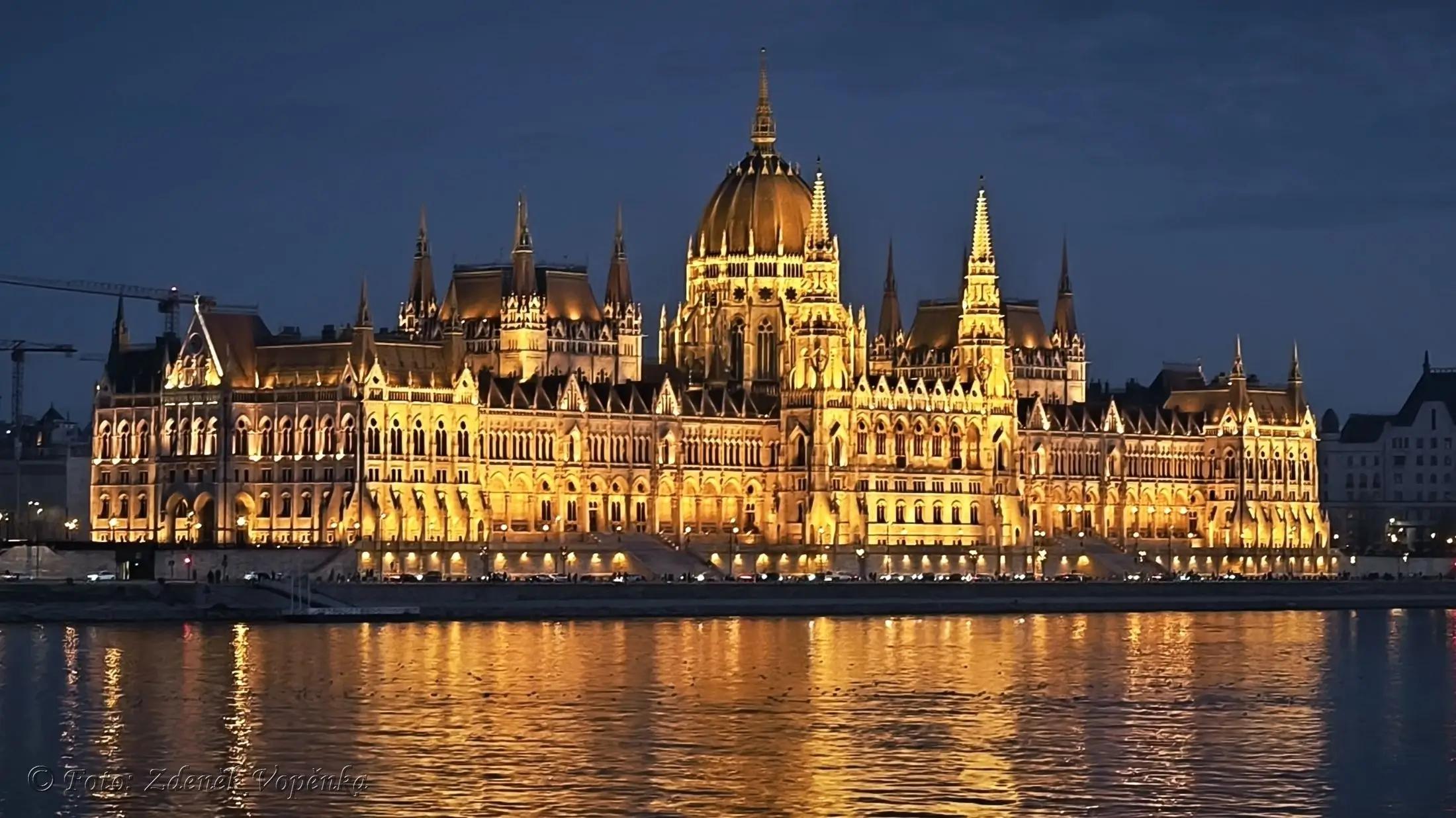 Letecký záběr na město Budapešť a jeho řeku za soumraku. Jde vidět budova parlamentu, která svítí.