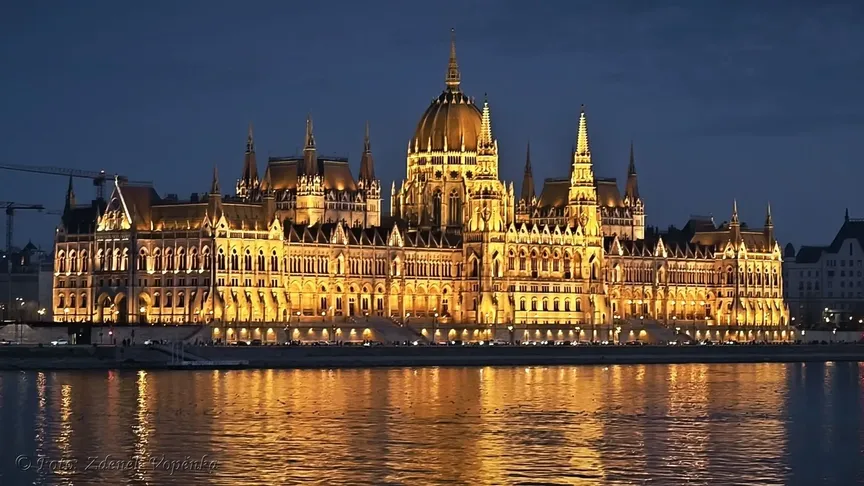 Letecký záběr na město Budapešť a jeho řeku za soumraku. Jde vidět budova parlamentu, která svítí.