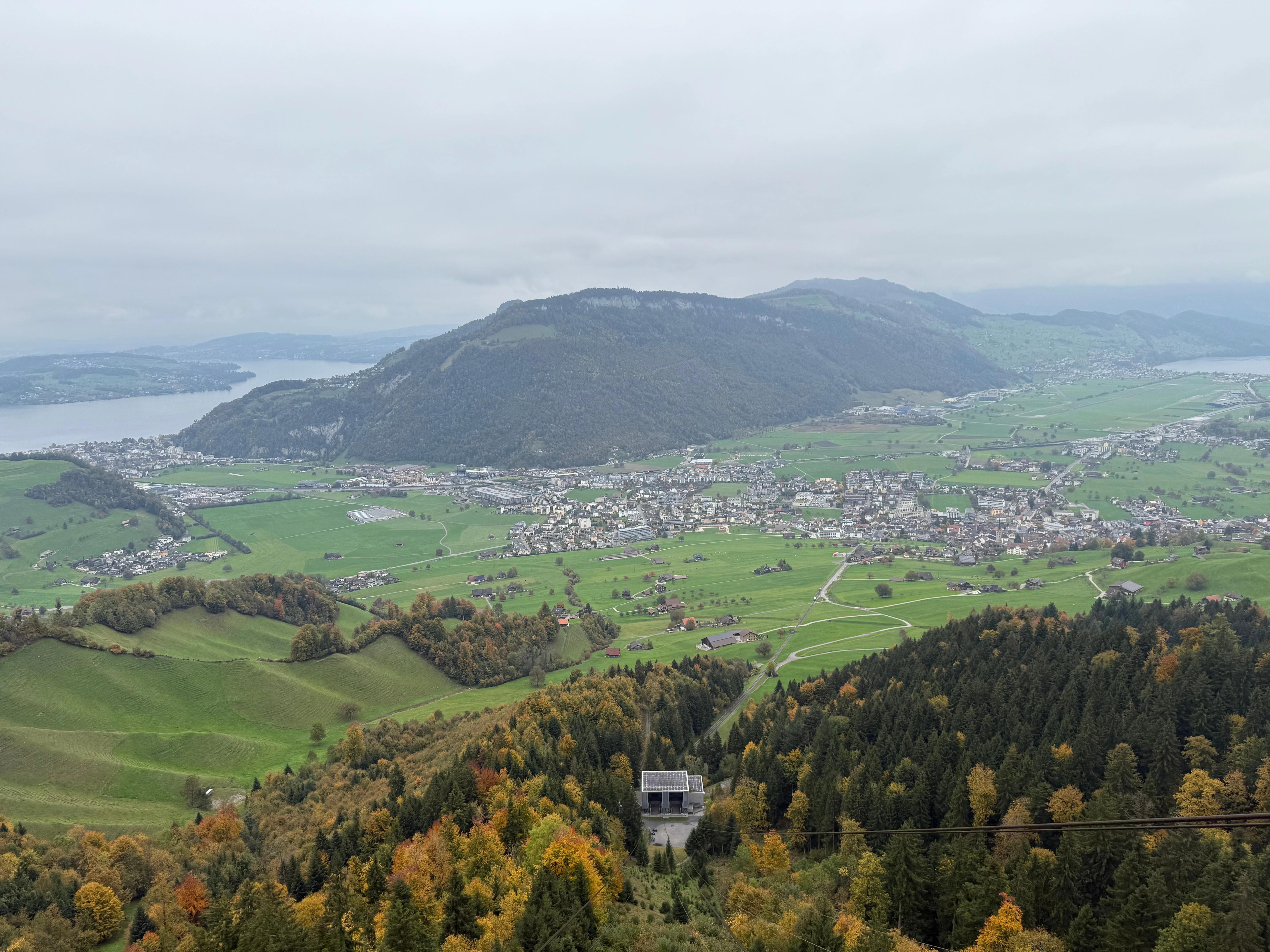 Panoramatický výhled na okolí hory Stanserhorn ve Švýcarsku-nacházející se zeleno-žluté stromy, louky, domy, hora a část vodní plochy