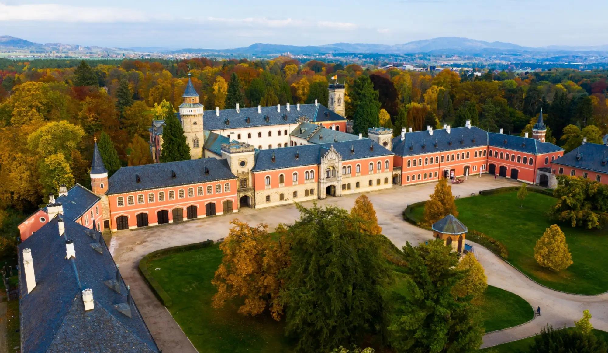 Zámek Sychrov z ptačí perspektivy, okolní stromy hrají podzimními barvami.