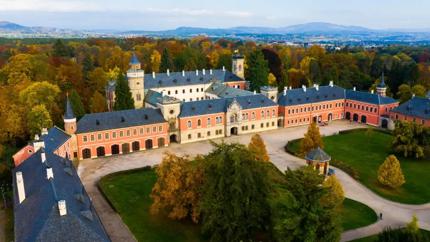 Zámek Sychrov z ptačí perspektivy, okolní stromy hrají podzimními barvami.