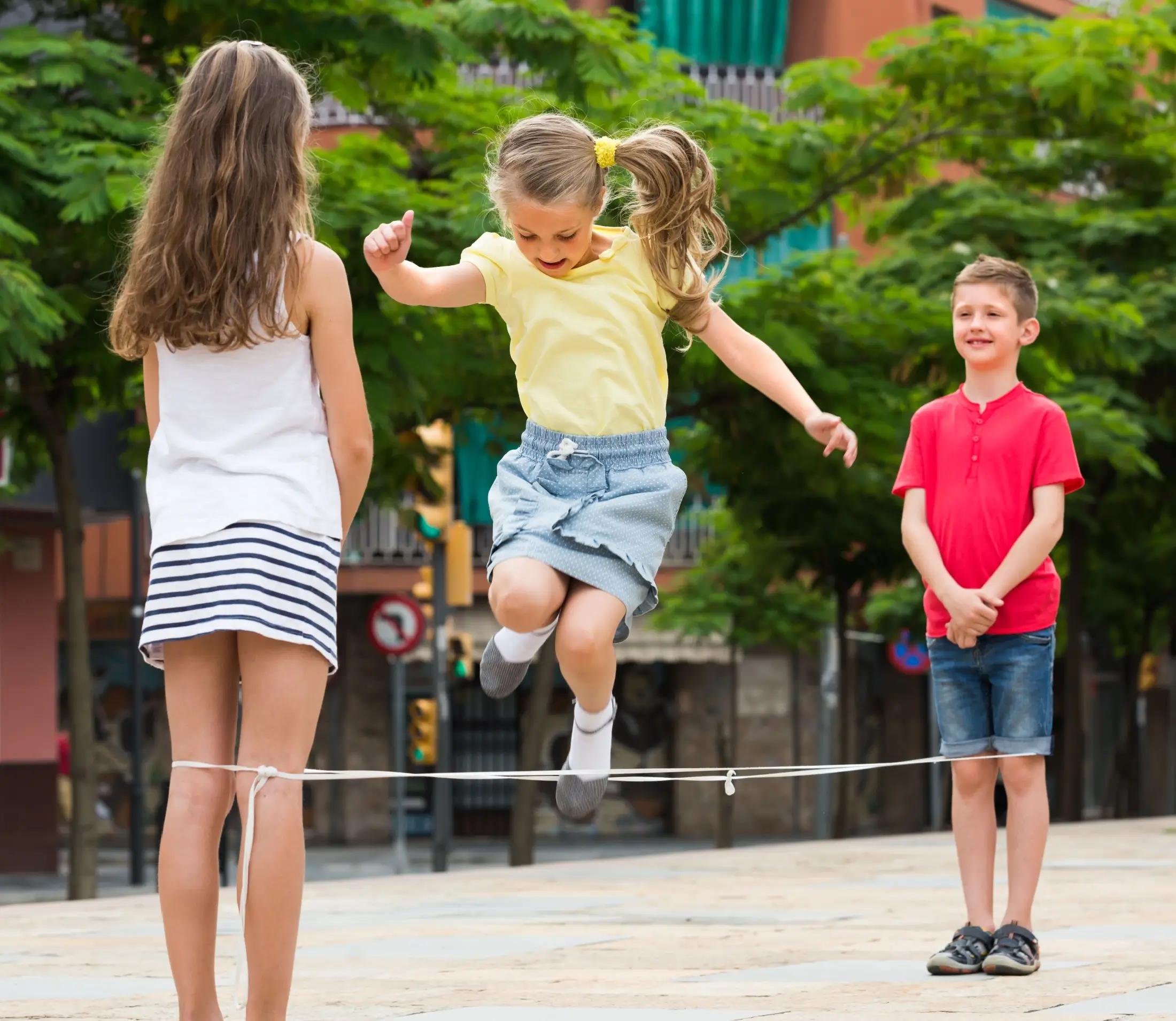 Na obrázku jsou tři děti, dvě dívky a jeden chlapec. Spolu hraji jednu z retro her - skákání přes gumu. 